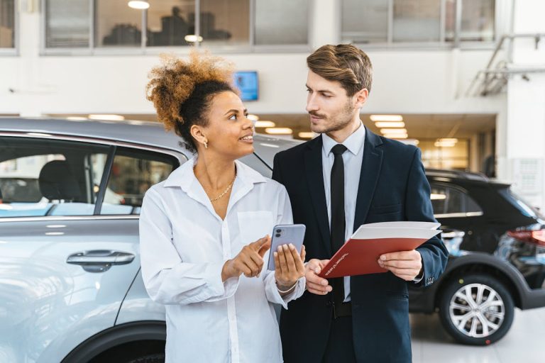 Woman with phone checking car history at a dealership with a car dealer